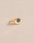 A gold ring shaped like an eye with a starry opal stone set in the center, on a neutral background.