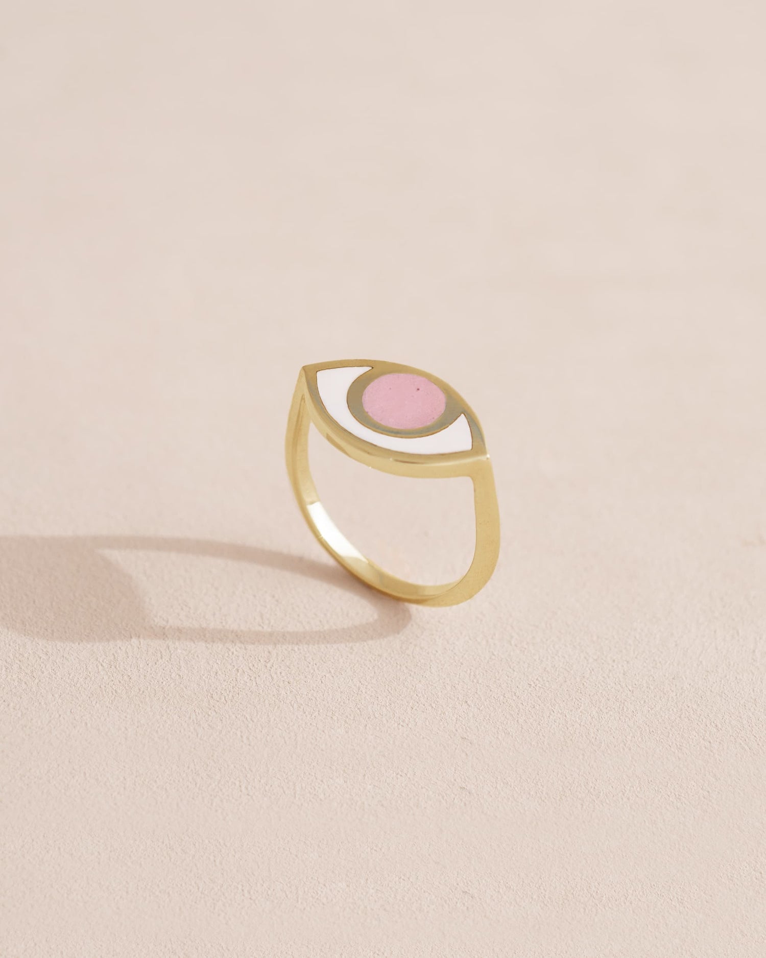 A gold ring with a pink opal centered on the top, placed on a light background.