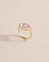 A gold ring with a pink opal centered on the top, placed on a light background.