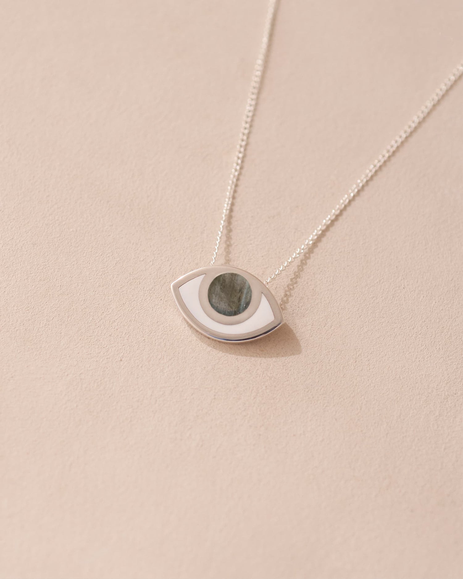 A silver pendant necklace with a labradorite stone in the shape of an eye, displayed against a beige background.