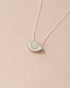 A silver pendant necklace with a round opal stone set in a eye-shaped frame, displayed against a light background.