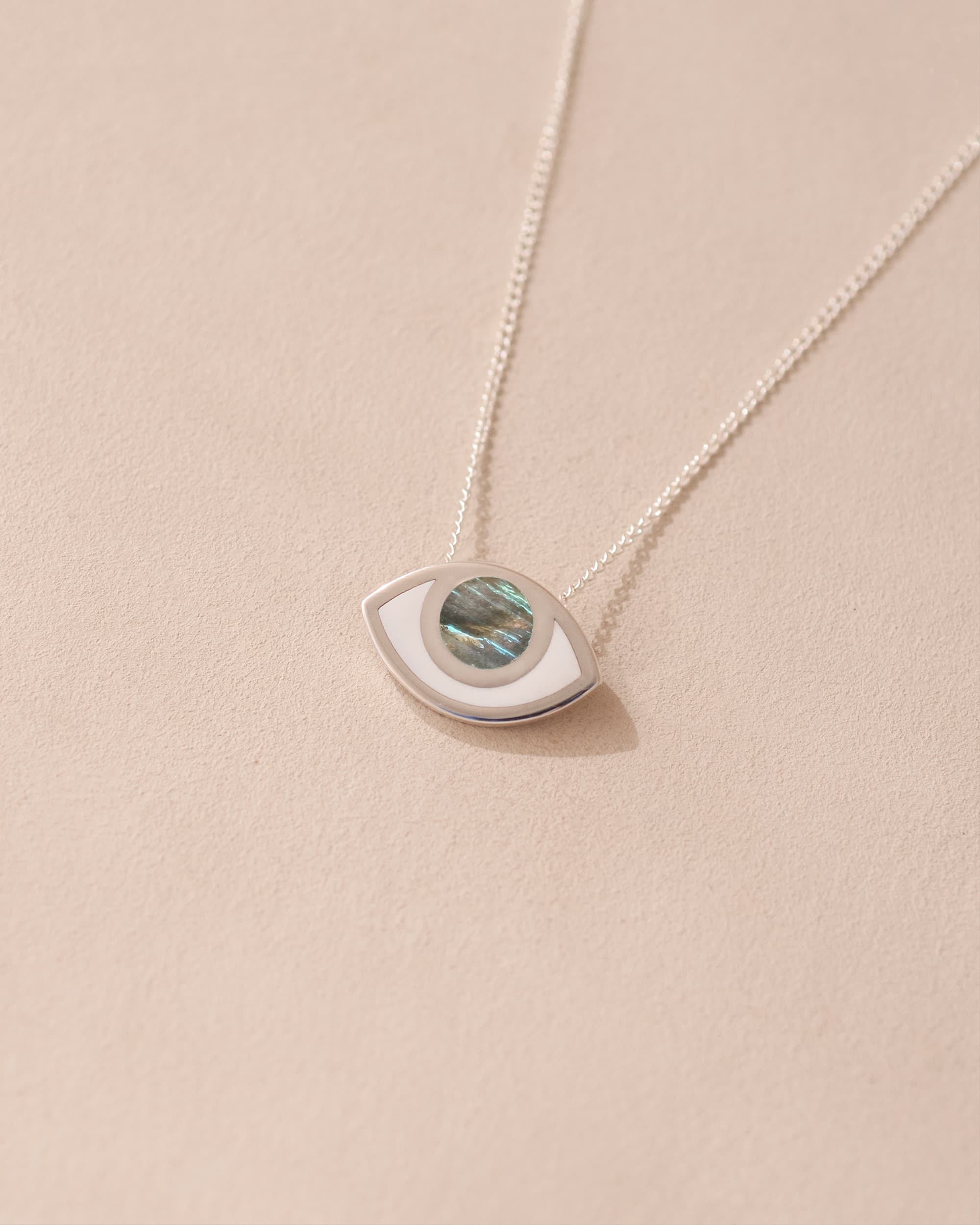 A silver pendant necklace with a labradorite stone in the shape of an eye, displayed against a light background.
