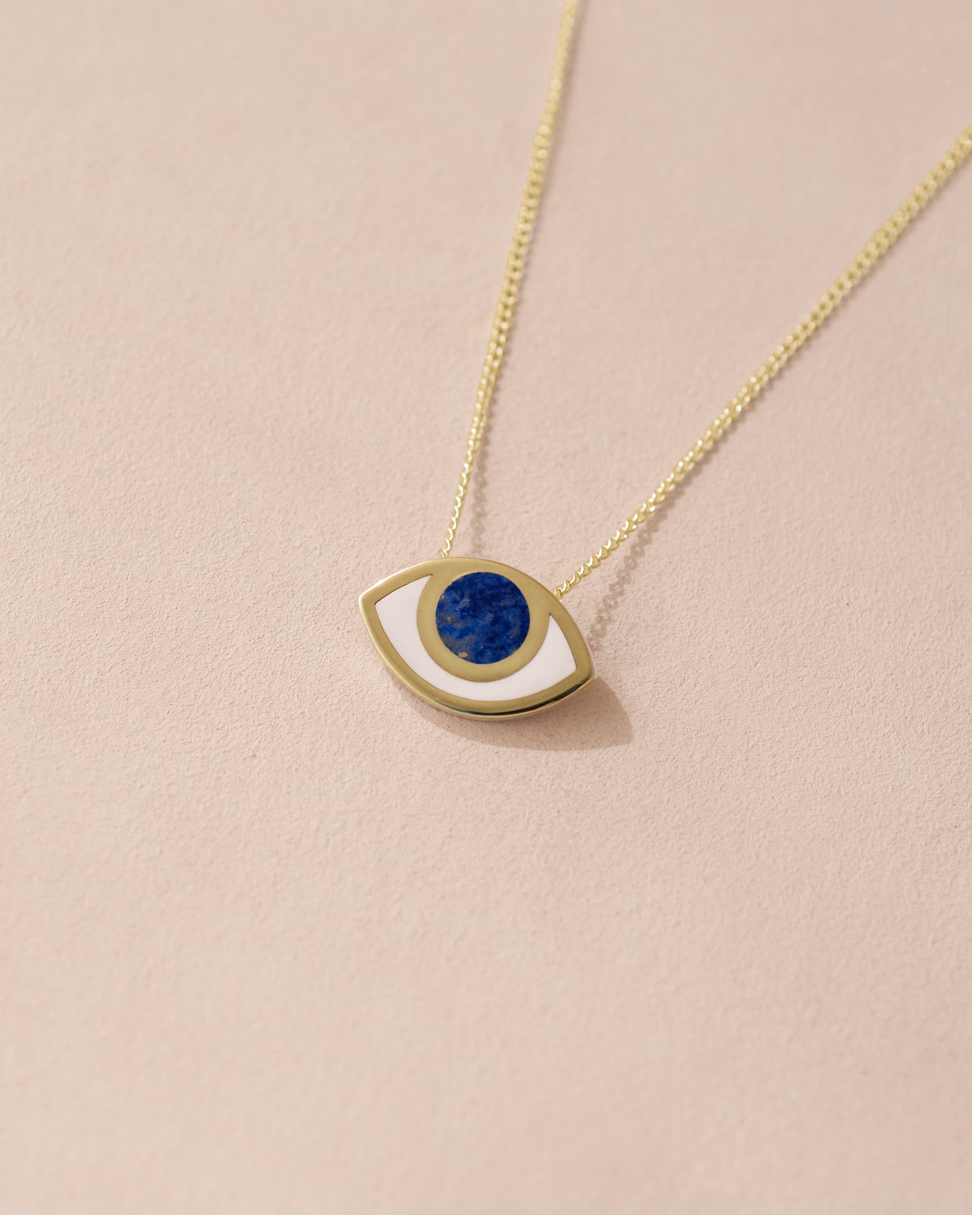 A 14K yellow gold pendant necklace with a lapis lazuli stone shaped as an eye, displayed against a light background.