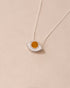 A silver pendant necklace with a round orange mookaite stone set in a eye-shaped frame, displayed against a beige background.