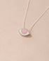 A silver pendant necklace with a pink opal eye design on a beige background.