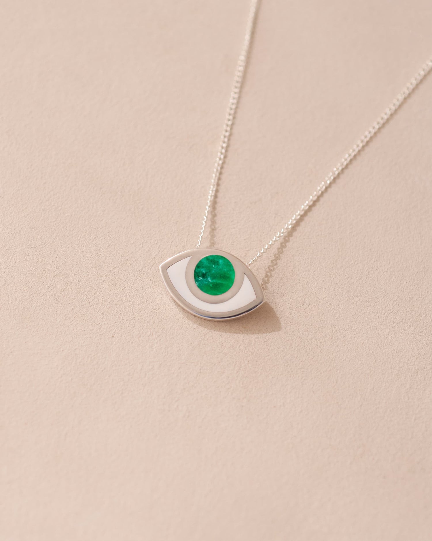 A silver pendant necklace with a variscite stone shaped like an eye, displayed against a beige background.