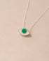A silver pendant necklace with a variscite stone shaped like an eye, displayed against a beige background.