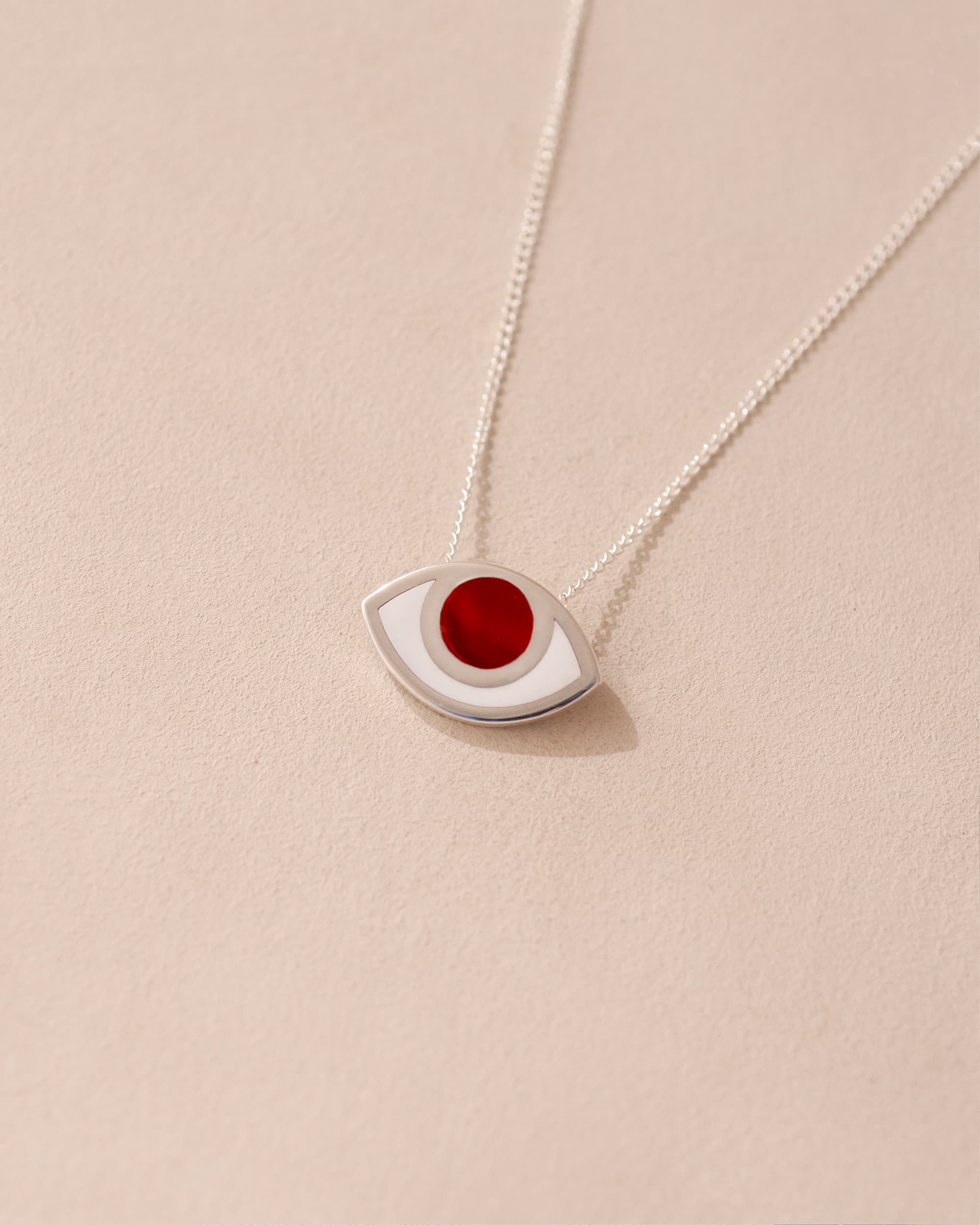 A silver pendant necklace with a carnelian stone in the shape of an eye, displayed against a light background.
