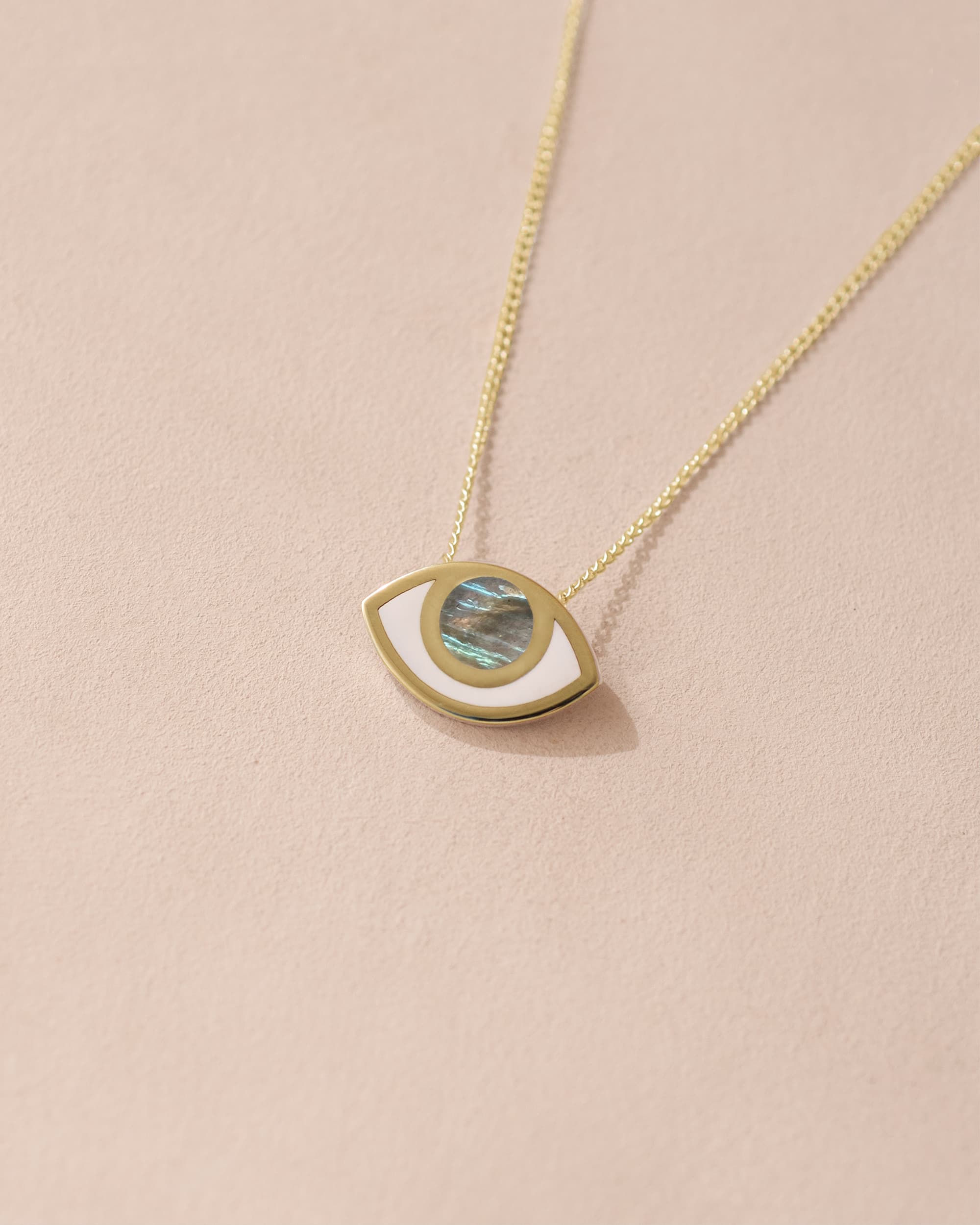 A pendant necklace with a gold eye design containing a labradorite stone, set against a light background.