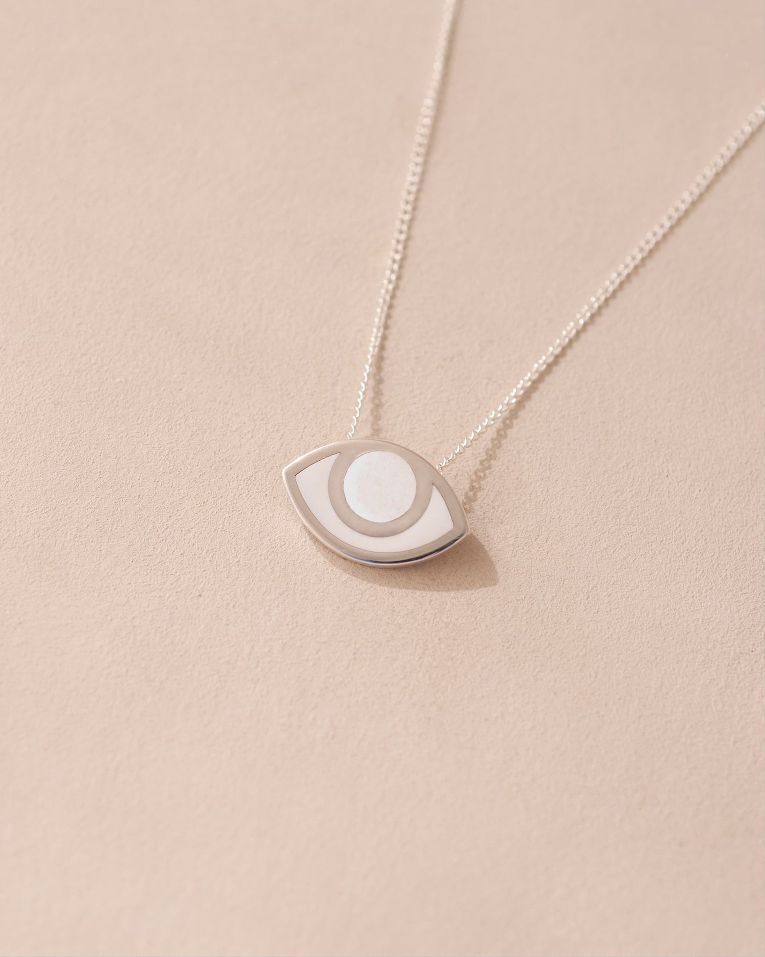 A silver pendant necklace with a porcelain eye design, displayed against a beige background.
