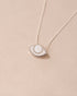 A silver pendant necklace with a porcelain eye design, displayed against a beige background.