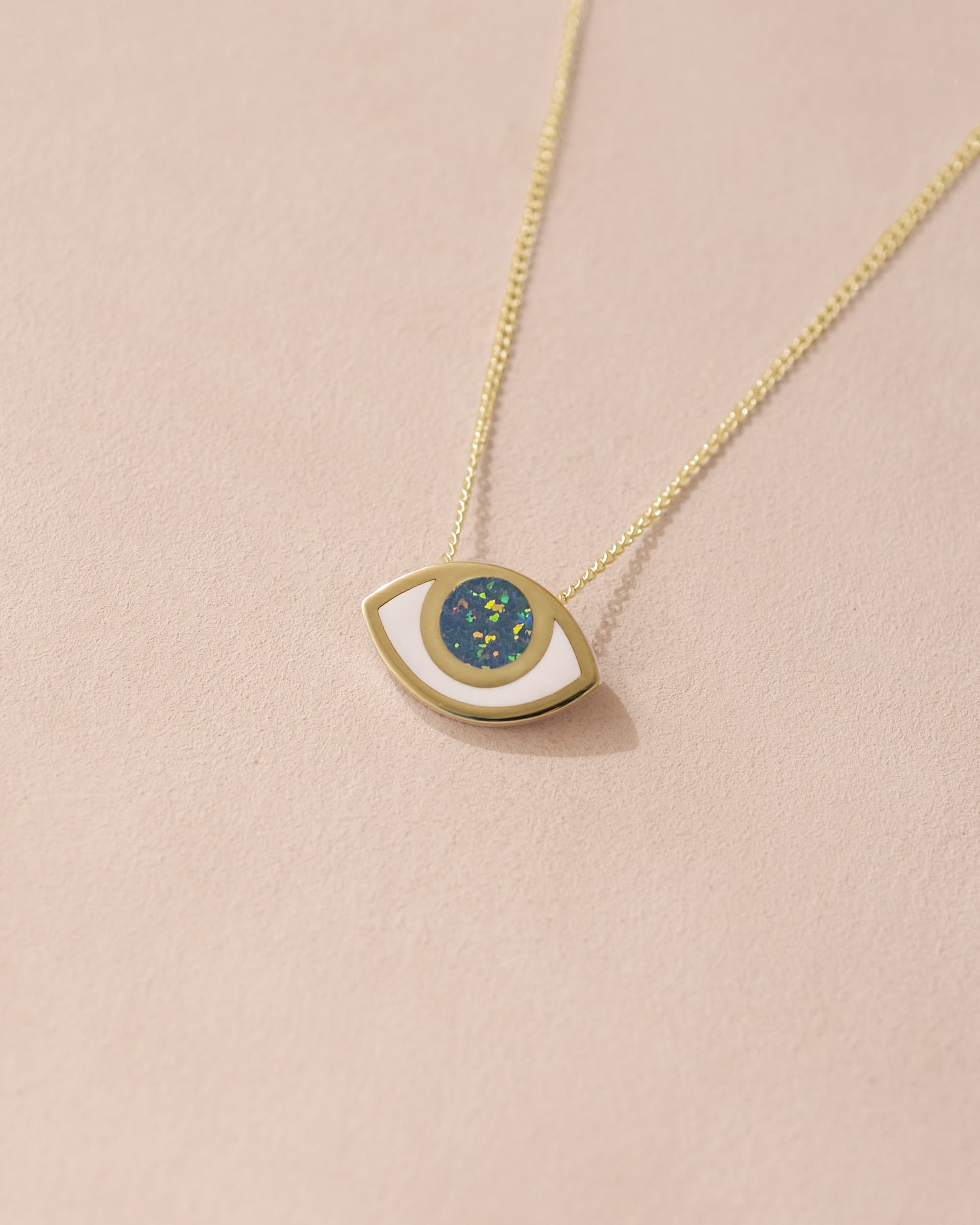 A 14K yellow gold pendant necklace with a gold chain and a geometric patterned eye design pendant, displayed against a light background.