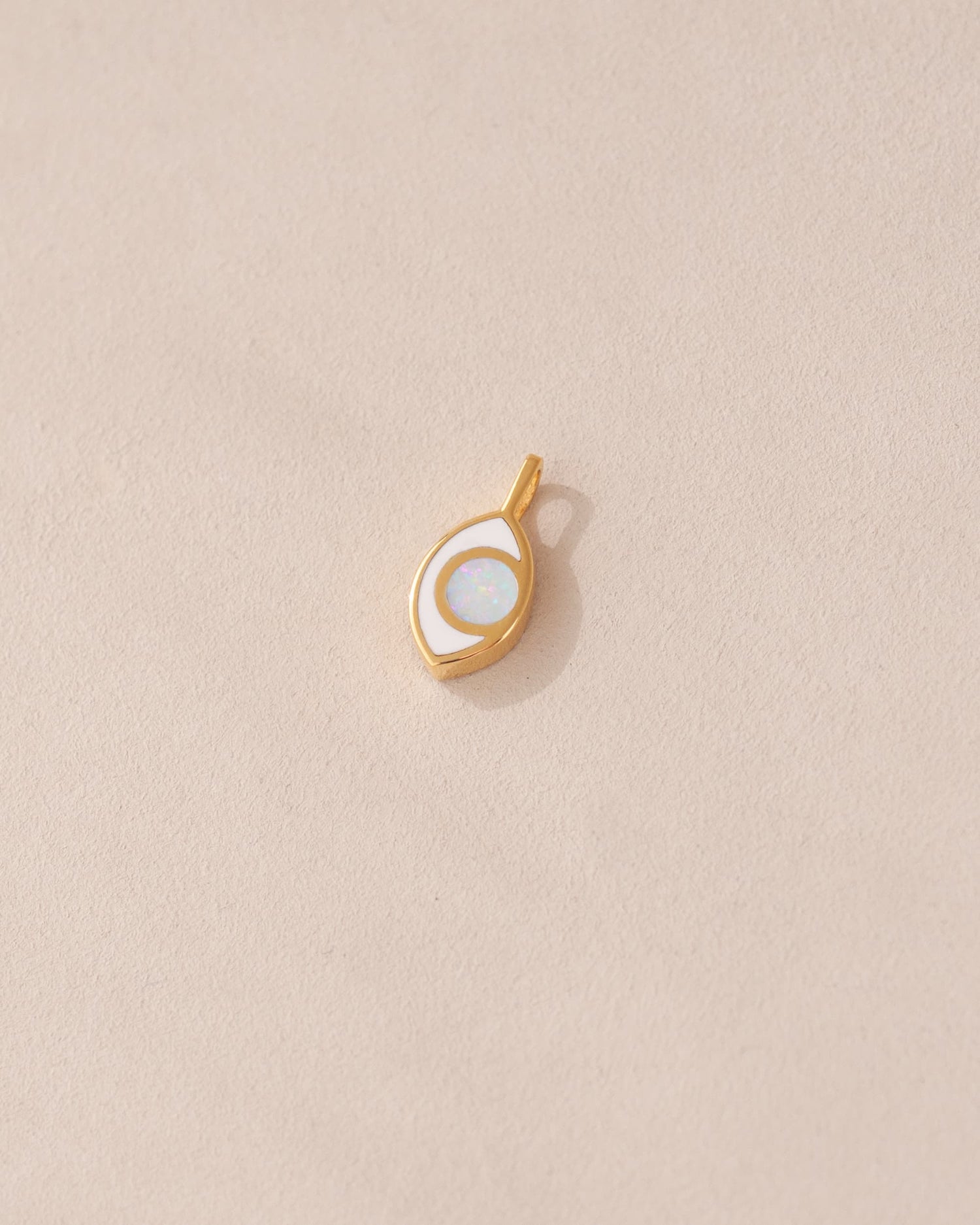 a gold charm shaped like an eye featuring a round opal center