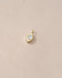 A small gold charm with an opal in the center, designed to resemble an eye, placed on a beige background.