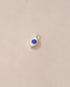 A silver charm with a lapis lazuli stone in the shape of an eye, placed against a beige background.