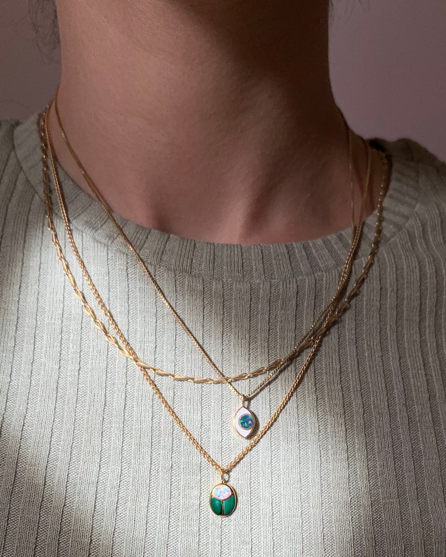 An eye shaped charm and a scarab charm layered on gold chains worn by a model