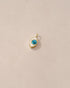 A small turquoise charm in the shape of an eye set in a gold frame, displayed against a beige background.