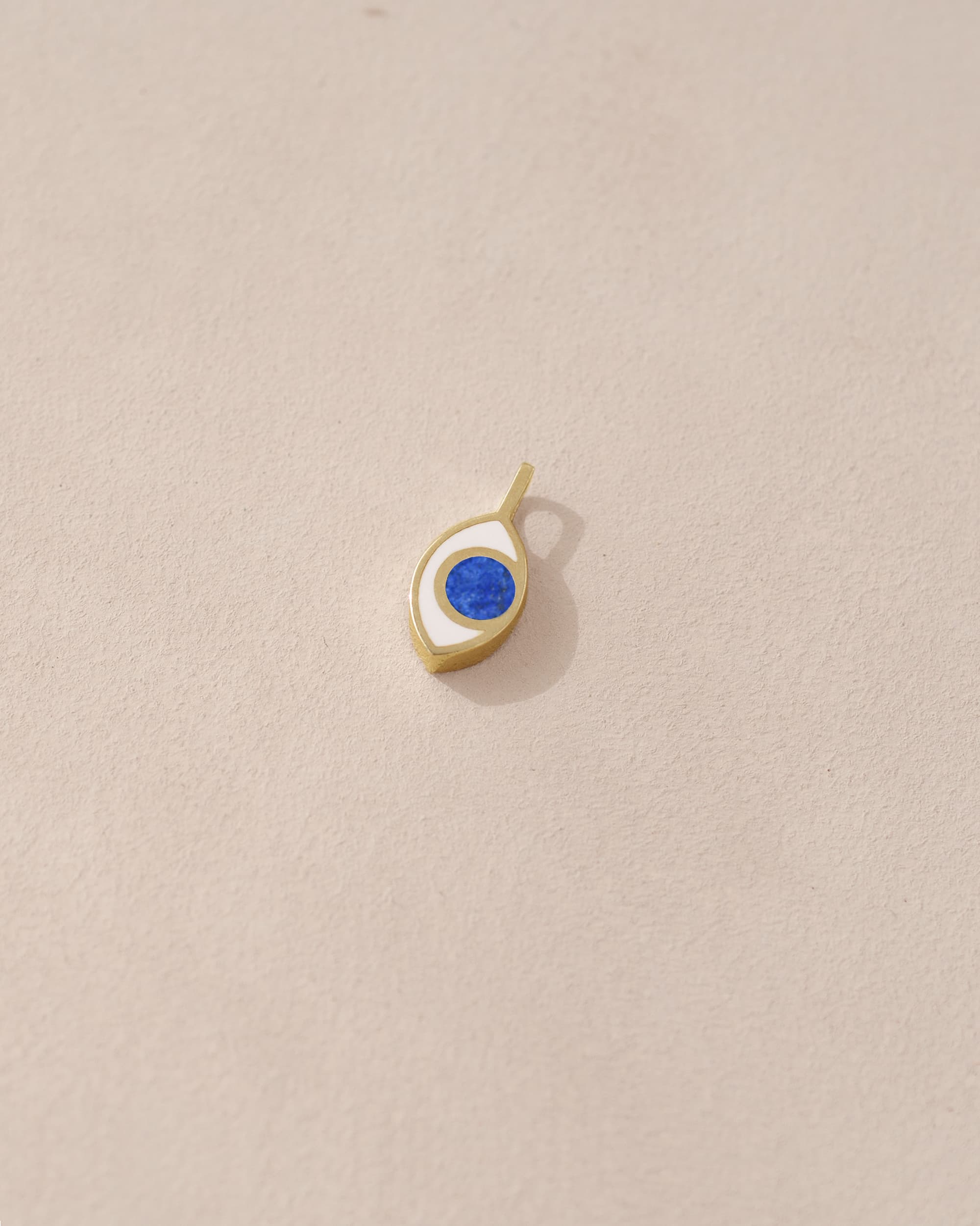A small lapis lazuli charm in a gold setting, shaped like an eye, placed against a beige background.