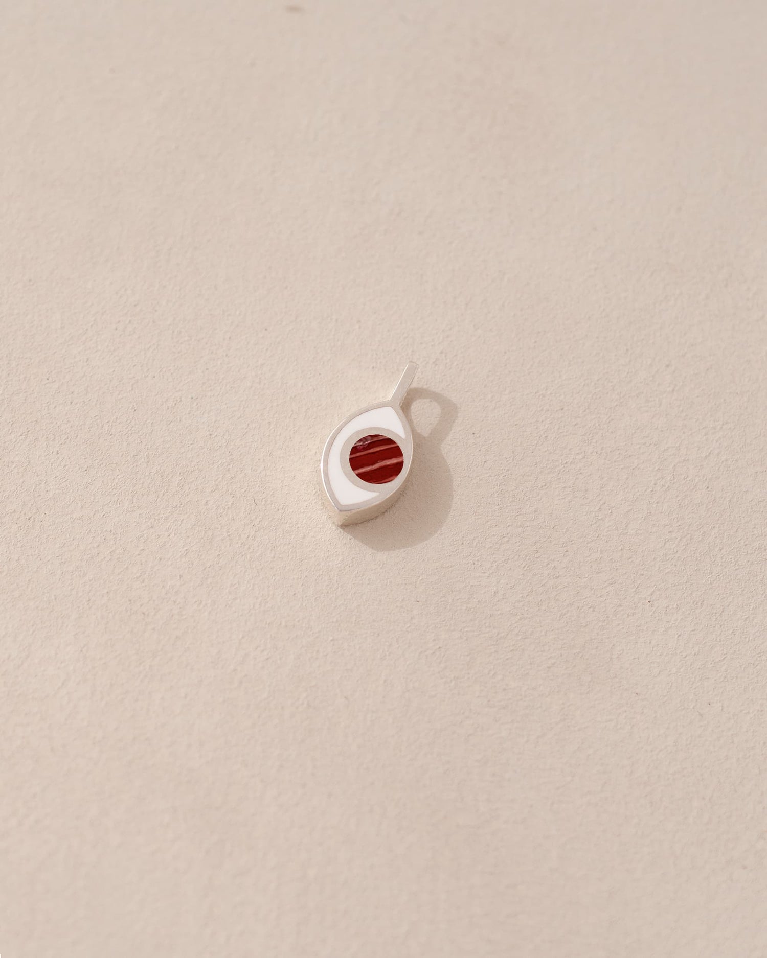A small silver charm with a jasper stone in the shape of an eye, placed on a light background.
