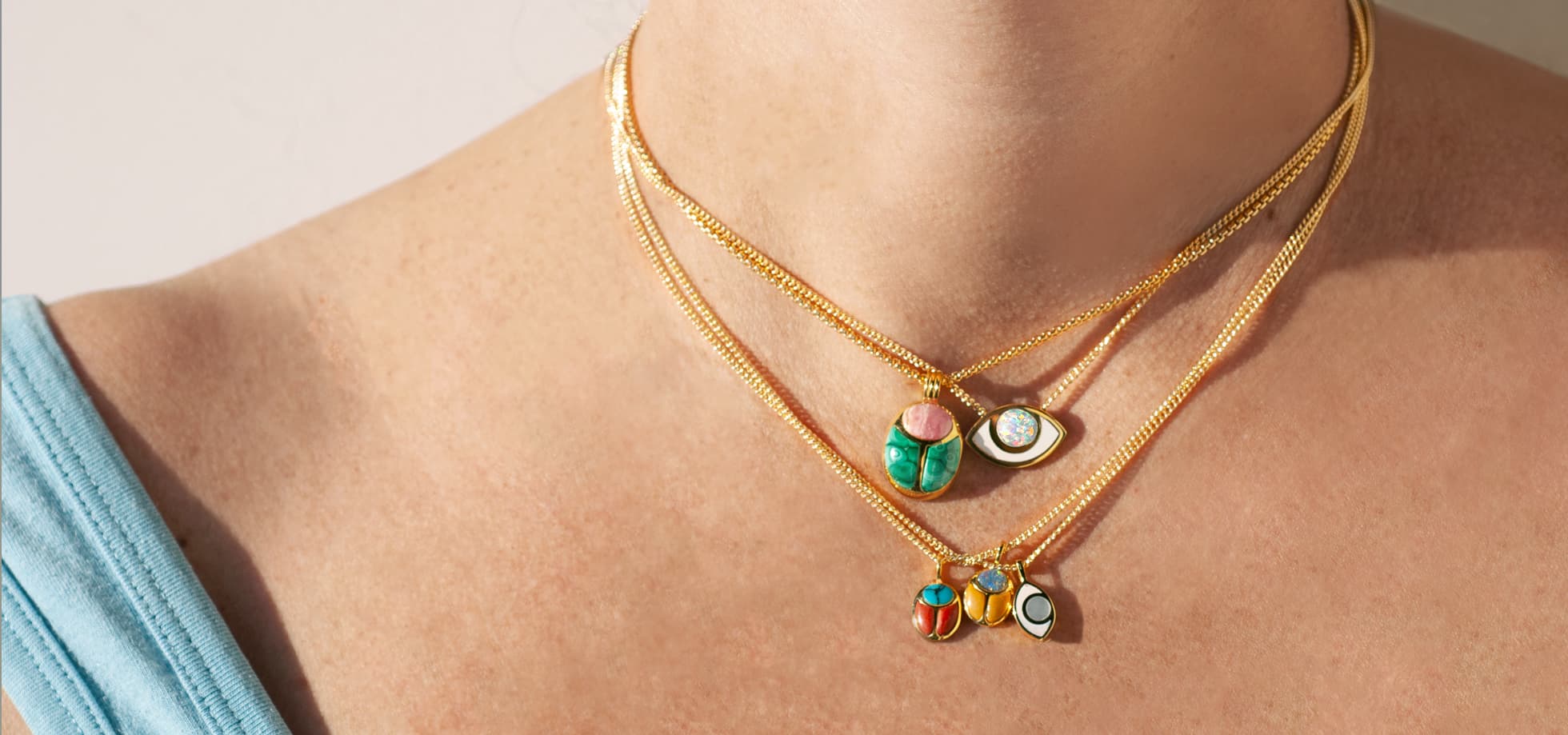 a model wearing multiple gold chains with gold eye shaped and scarab shaped charms and pendants hanging from them