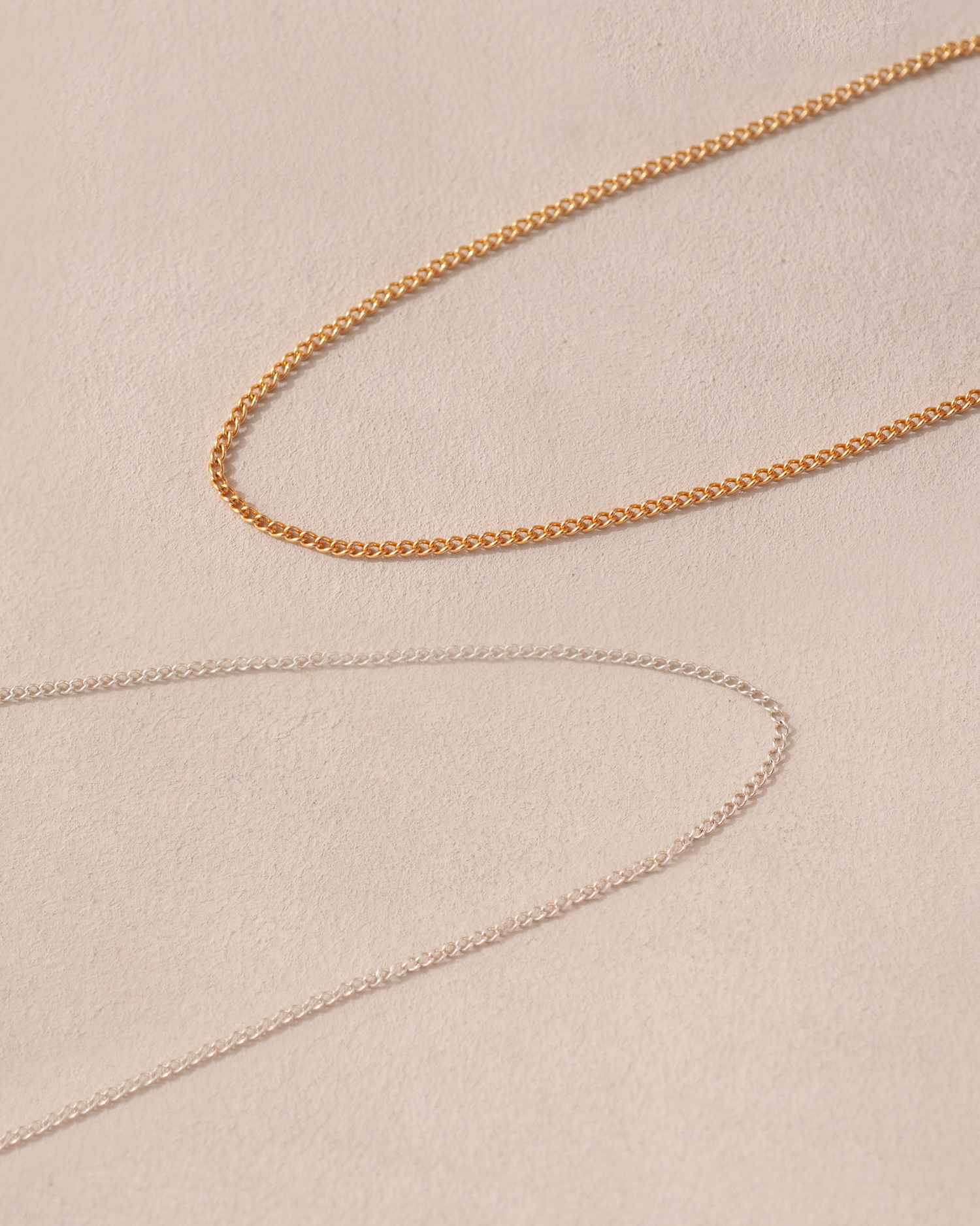 A close-up image of a 14K yellow gold curved chain necklace laid out on a textured background.