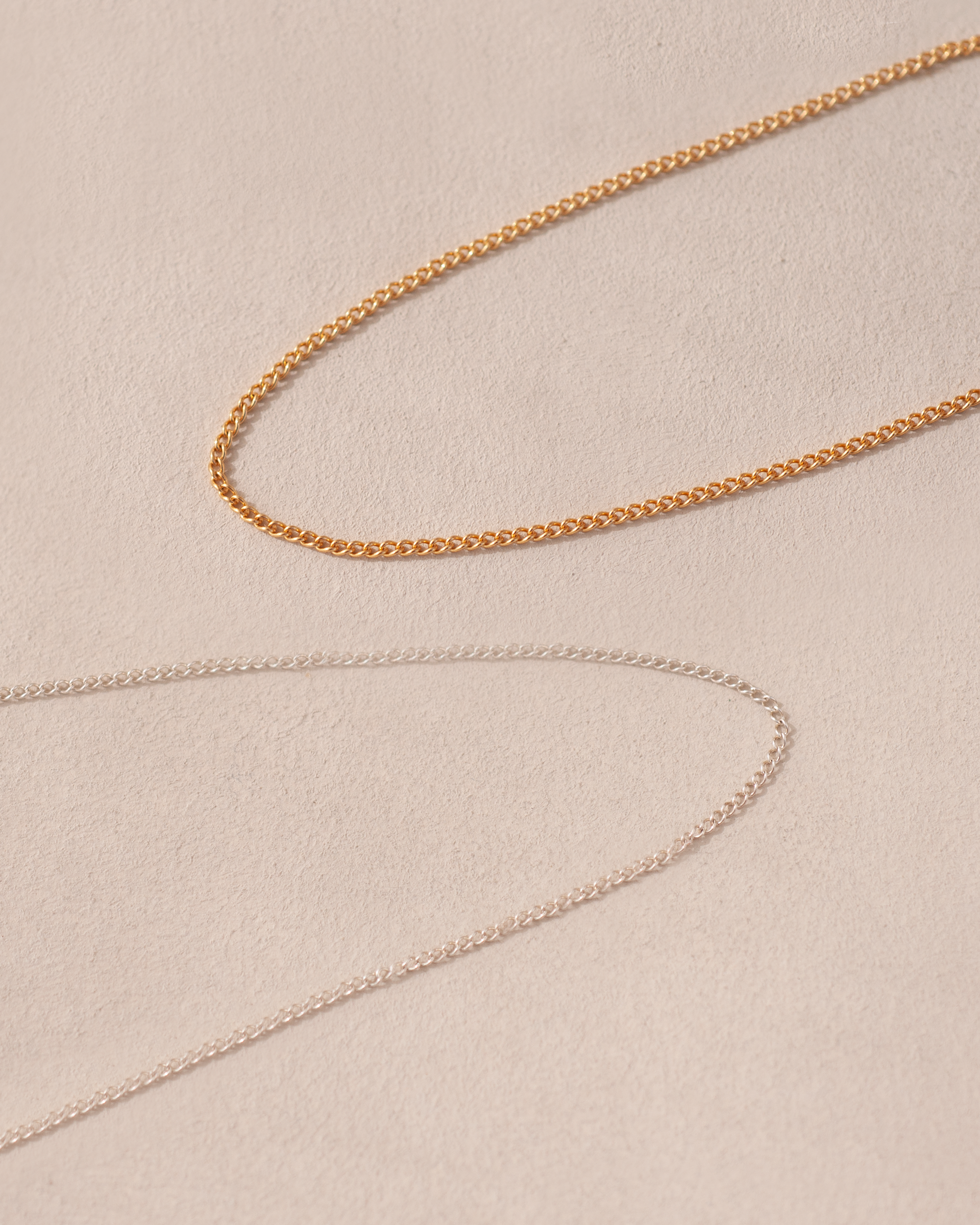 A close-up image of a 14K yellow gold curved chain necklace laid out on a textured background.