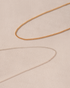 A close-up image of a 14K yellow gold curved chain necklace laid out on a textured background.