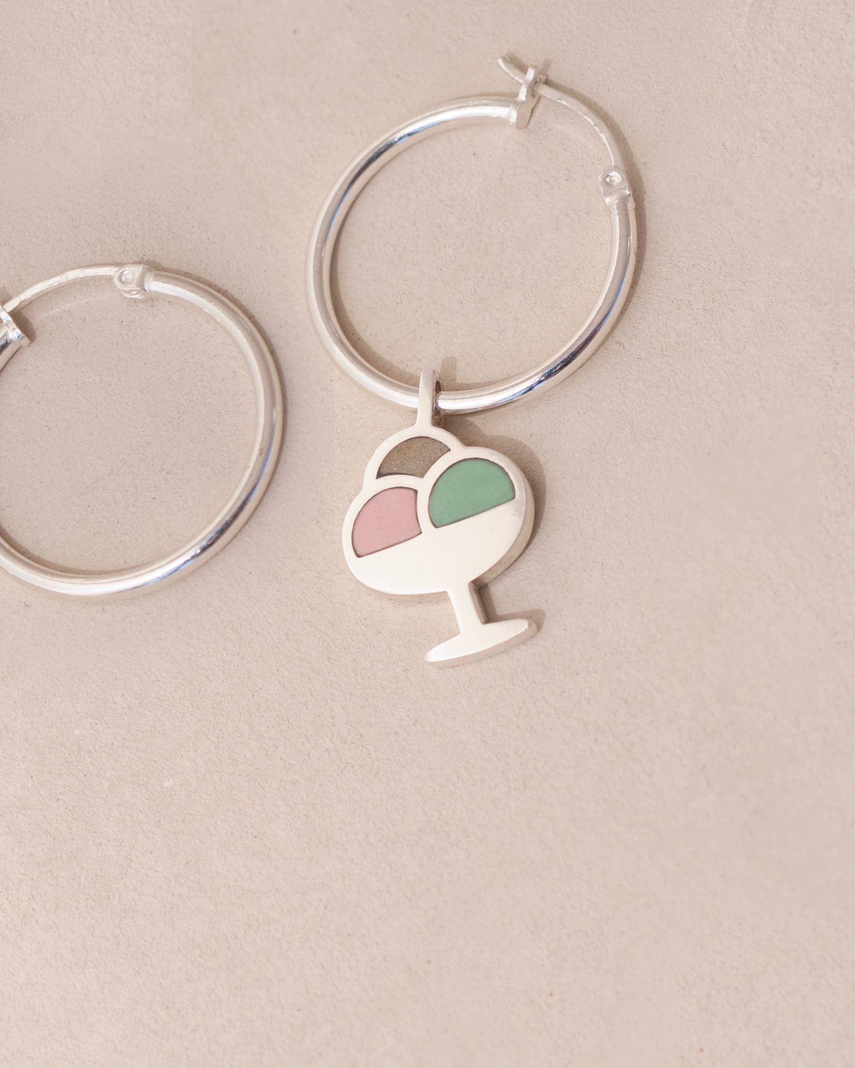 Silver hoop earrings with a heart and ice cream cone charm on a beige background