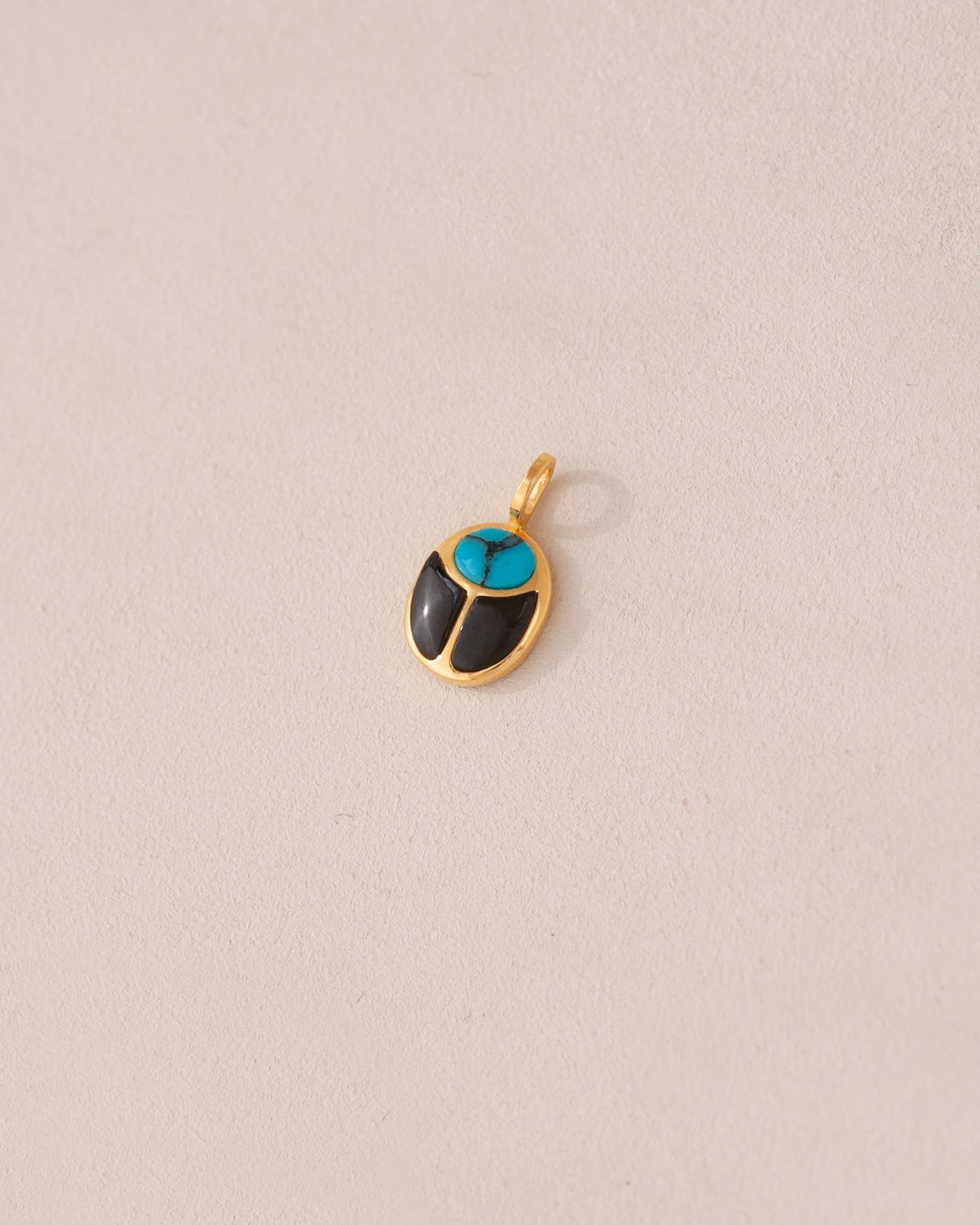 A 14K yellow gold charm in the shape of a scarab amulet with turquoise and onyx inlays, displayed against a neutral background.