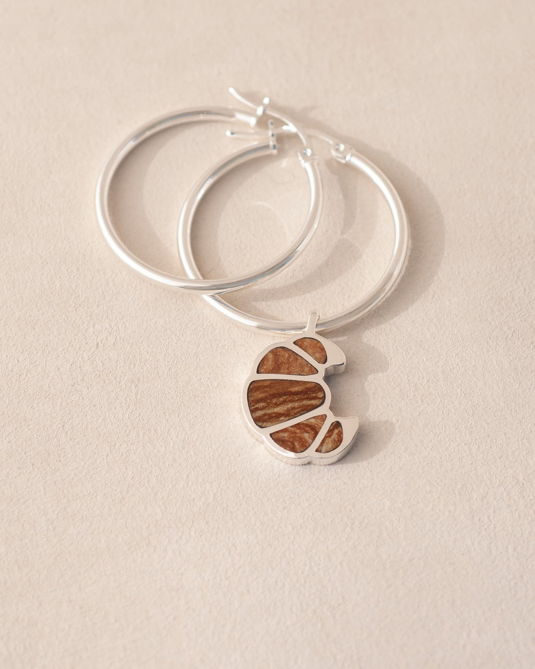 a silver charm shaped like a croissant, inlaid with jasper, dangling from silver hoops