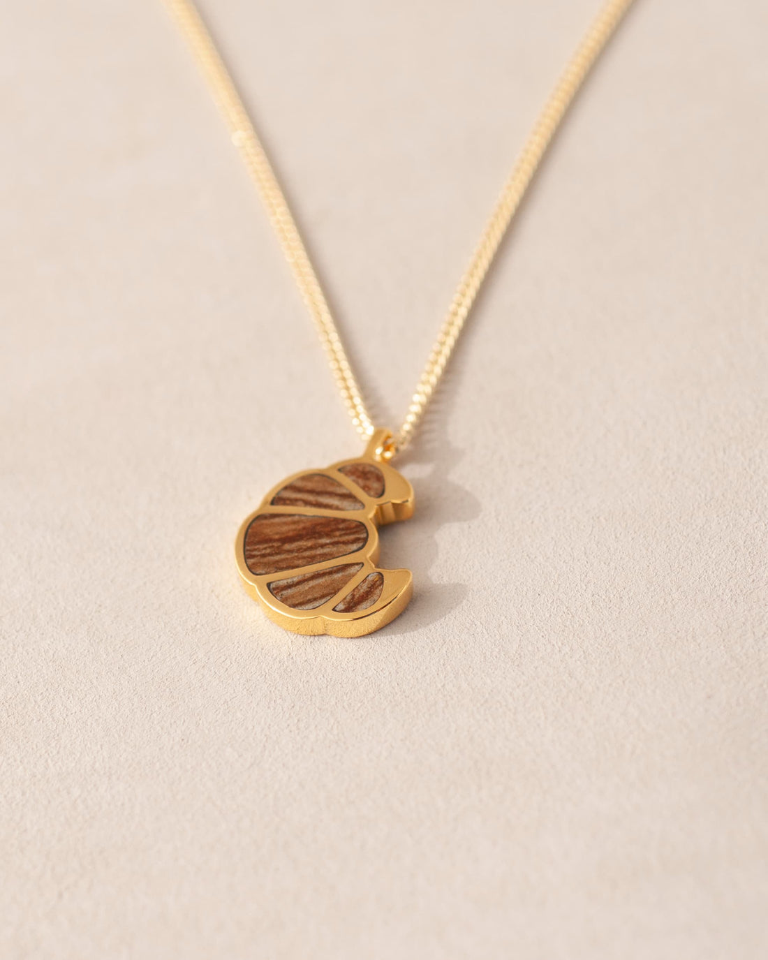 a gold charm shaped like a croissant dangling from a gold chain
