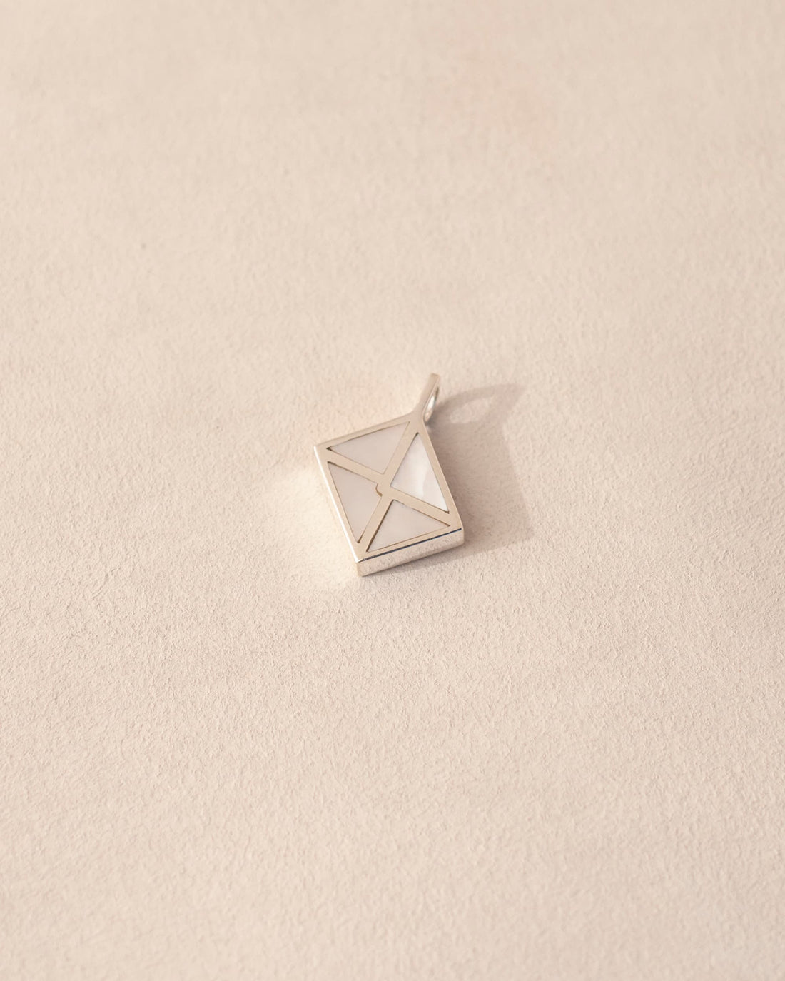 A silver envelope-shaped charm with mother of pearl inlay placed on a beige background