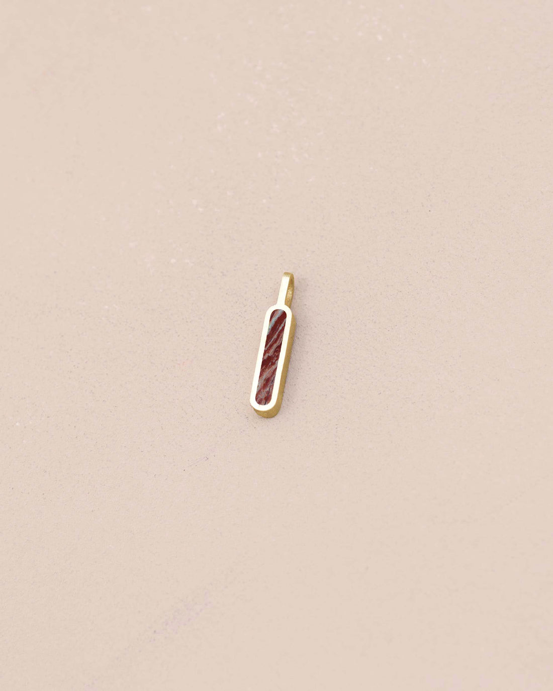 Gold pendant with a red stone on a beige background