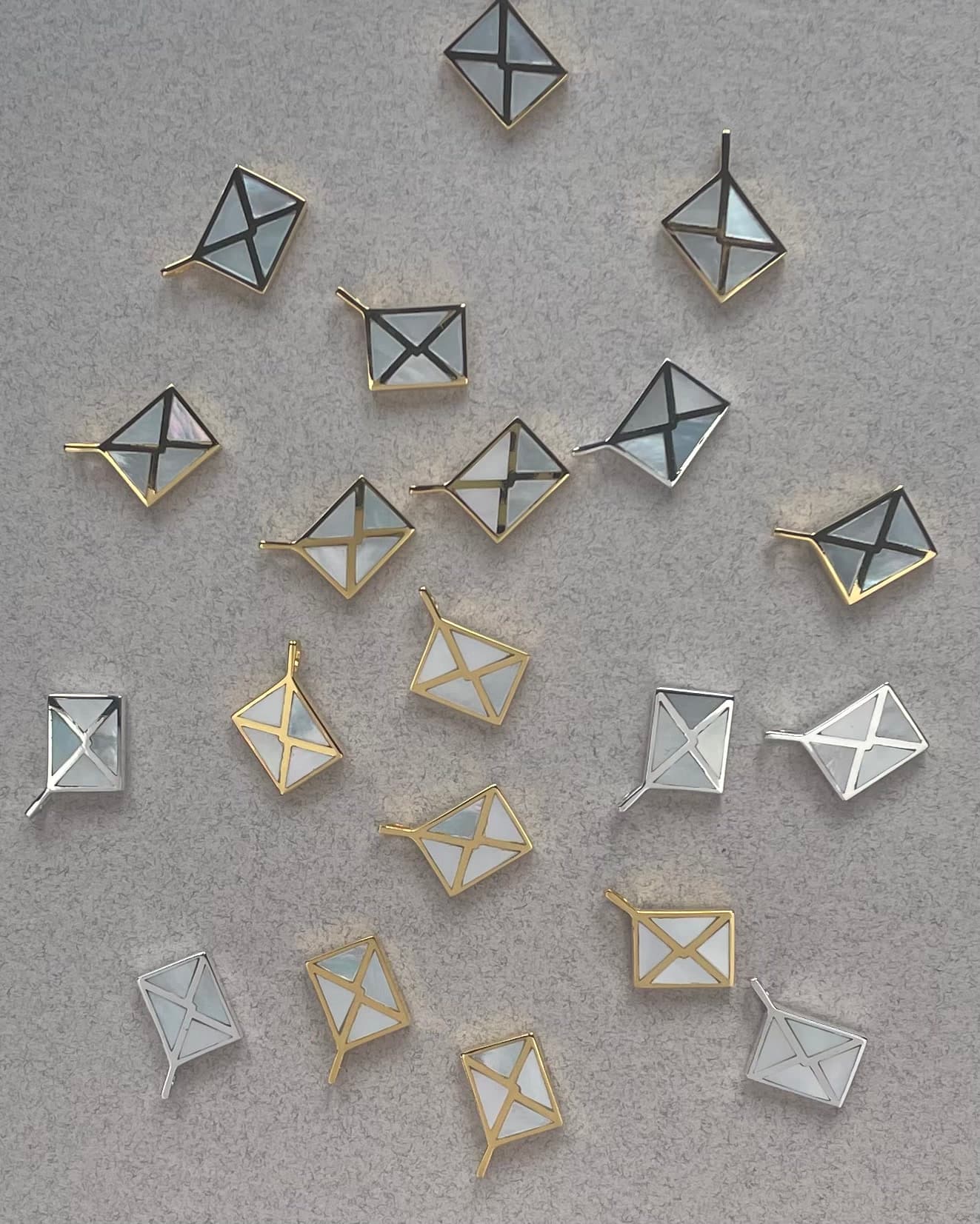 many silver and gold envelope charms inlayed with mother of pearl laying on a textured background