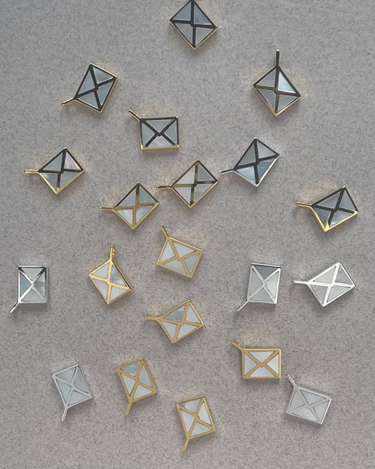 many silver and gold envelope charms inlayed with mother of pearl laying on a textured background