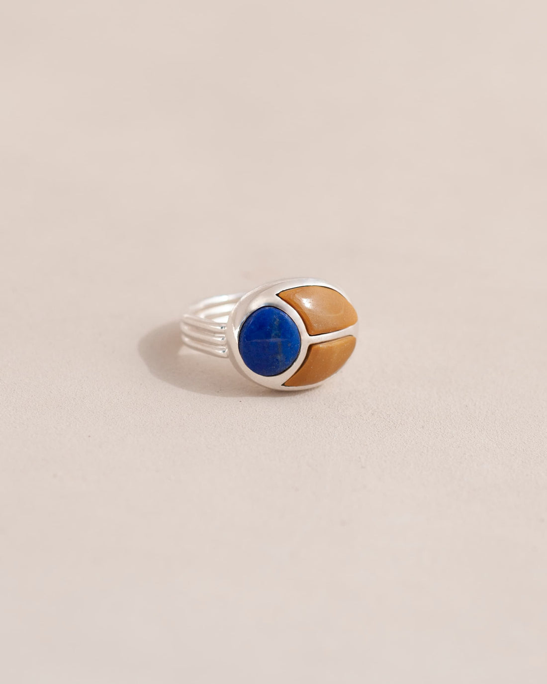 A silver ring featuring a scarab design with lapis lazuli and yellow opal inlays, displayed against a neutral background.