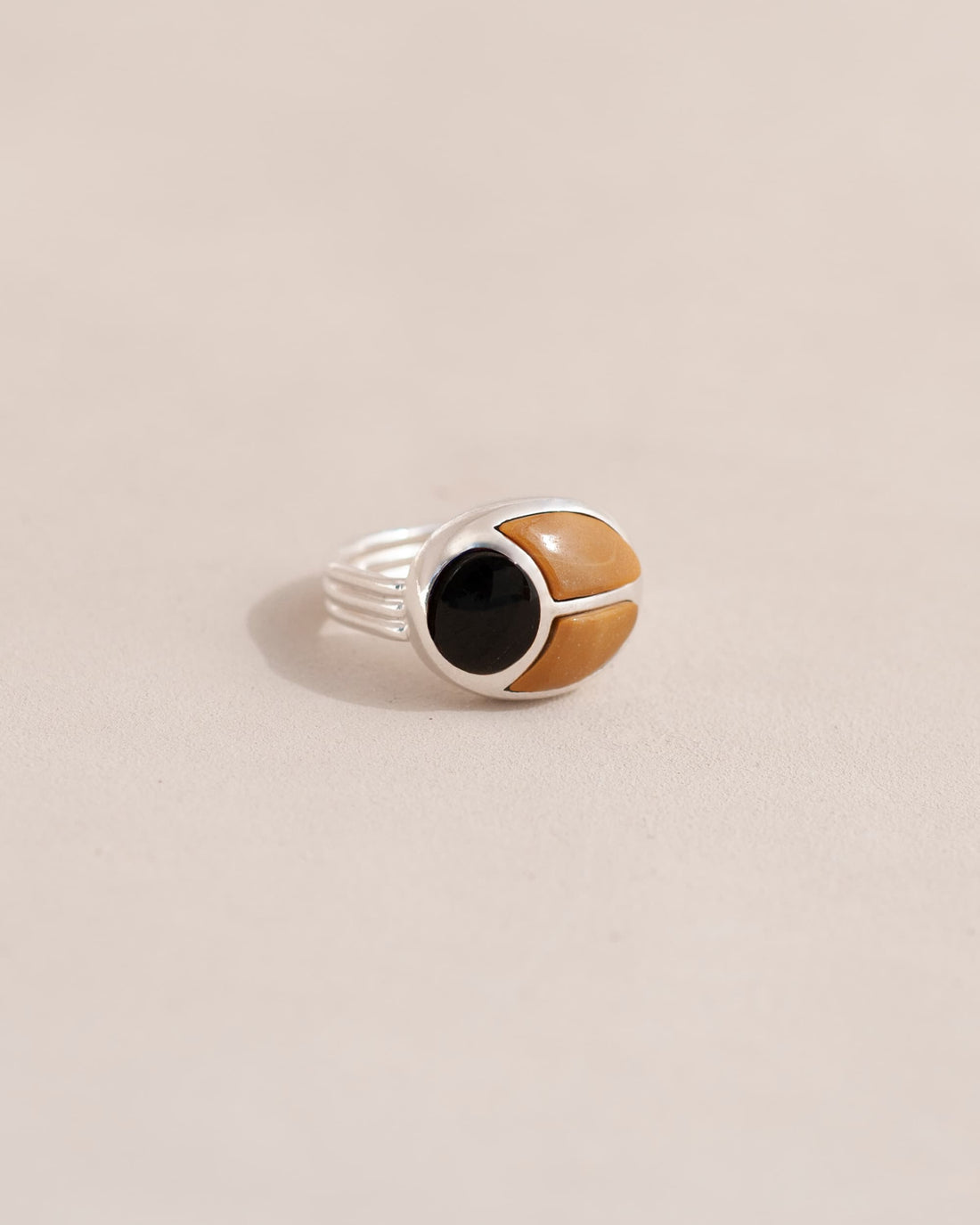A silver ring featuring a scarab design with onyx and yellow opal, displayed against a neutral background.