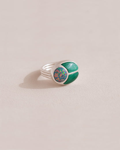 A silver ring featuring a central opal stone flanked by malachite stones on either side, set against a neutral background.