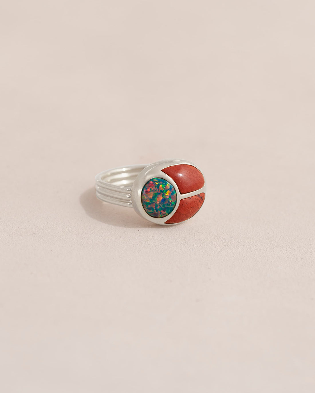 A silver ring featuring a scarab design with starry opal and red jasper inlays, displayed against a neutral background.