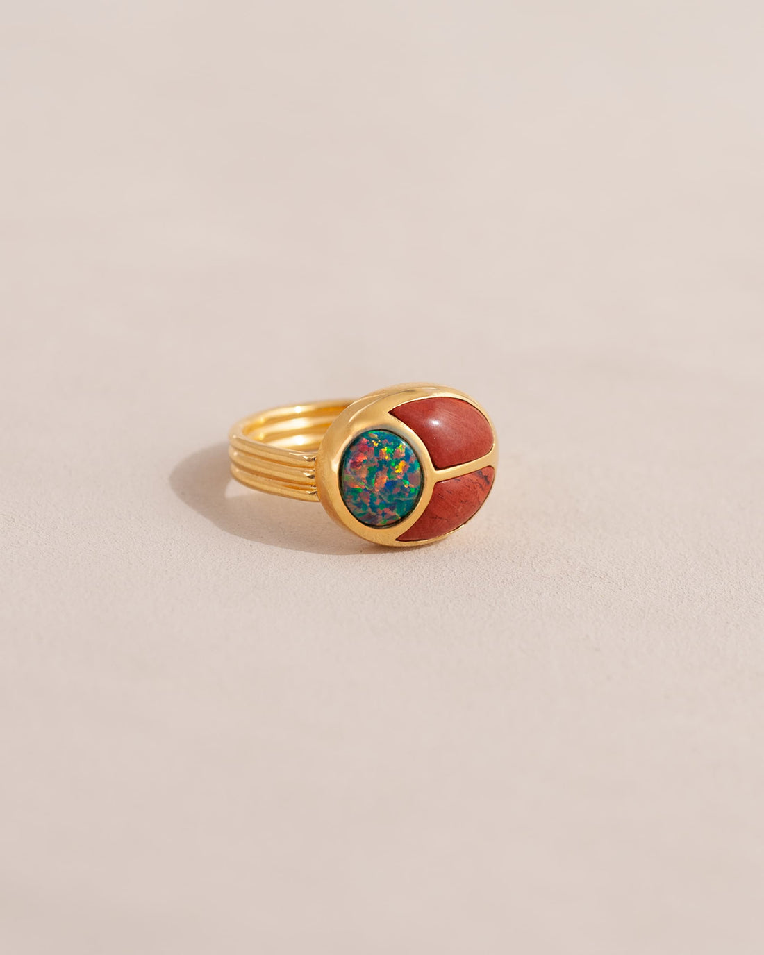 A gold ring featuring a scarab design with starry opal and red jasper inlays, displayed against a neutral background.