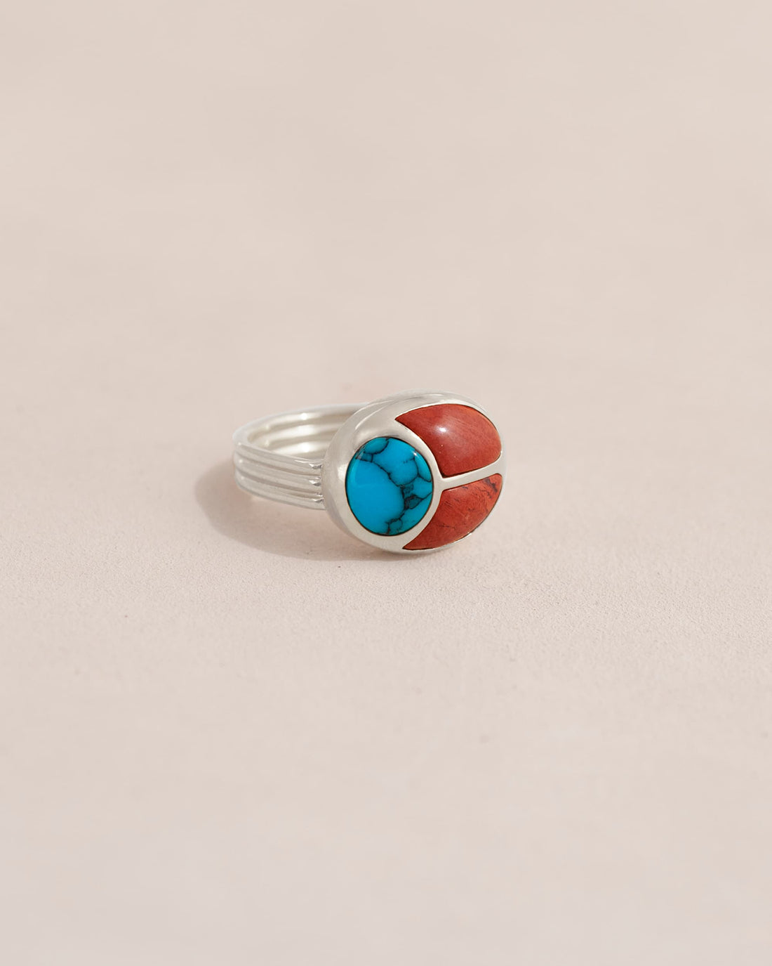 A silver ring featuring a scarab design with turquoise and red jasper inlays, displayed against a neutral background.