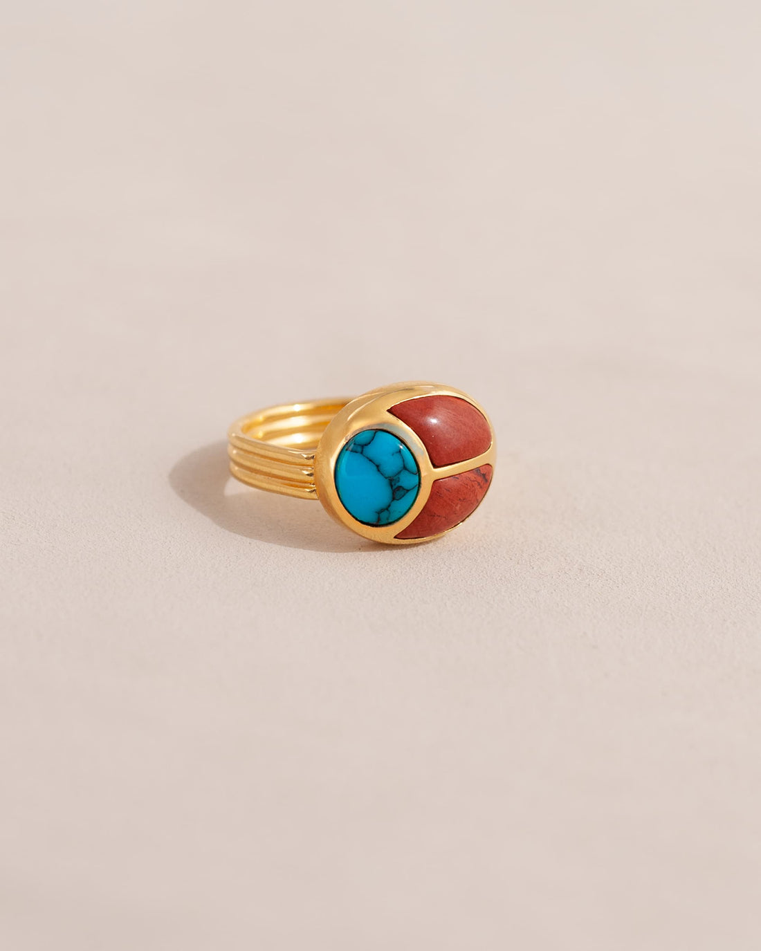 A gold ring featuring a scarab design with turquoise and red jasper inlays, displayed against a neutral background.