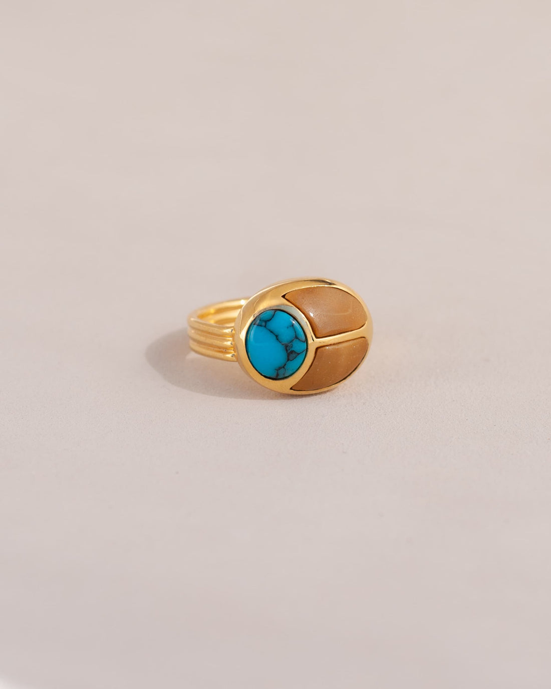 A gold ring featuring a scarab design with turquoise and yellow opal inlays, displayed against a neutral background.