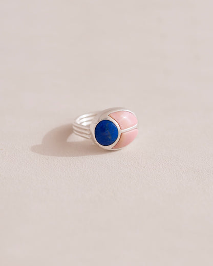A silver ring featuring a central lapis lazuli stone flanked by pink opal stones on either side, set against a neutral background.