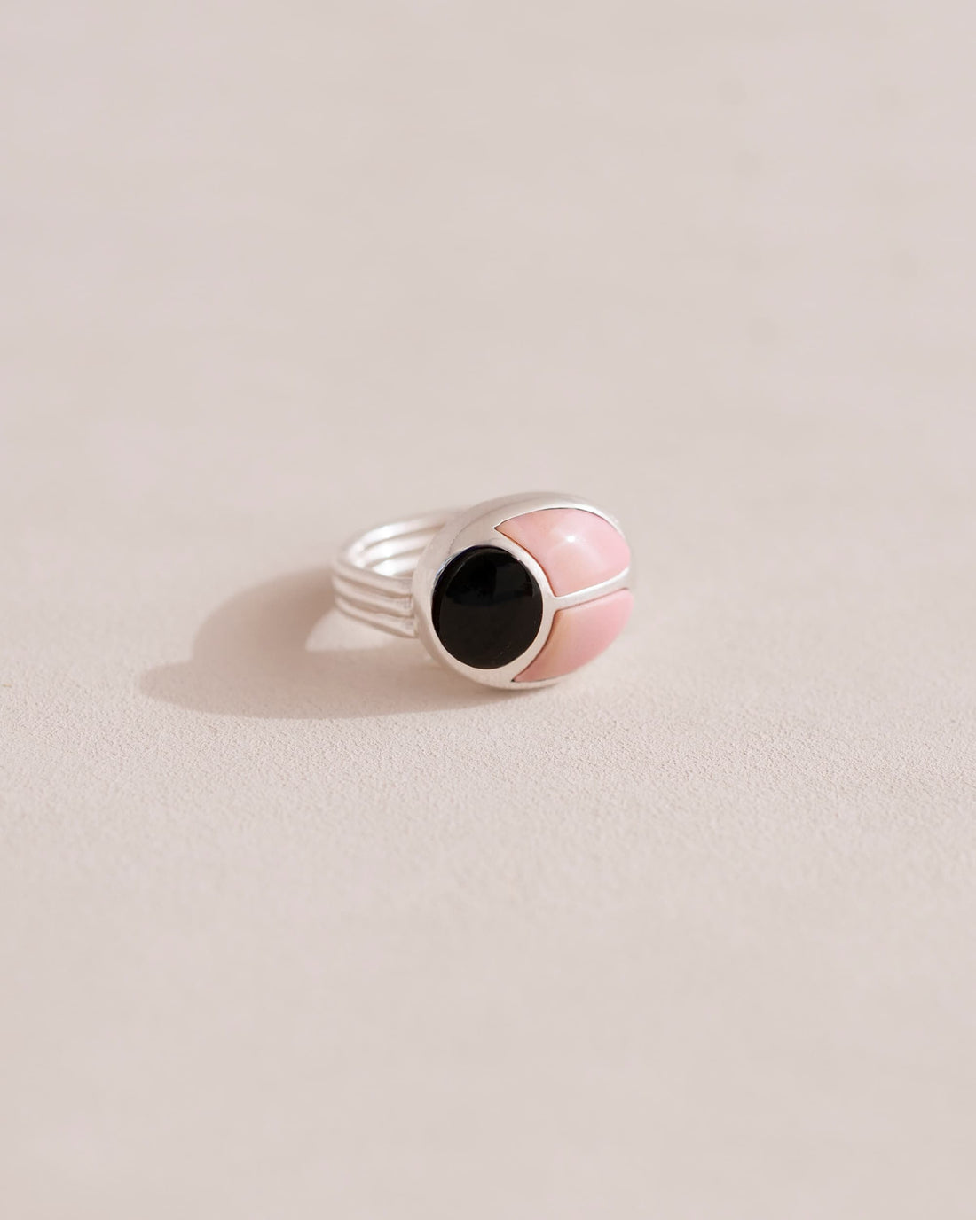 A silver ring with a pink opal center and surrounding onyx, placed on a plain background.