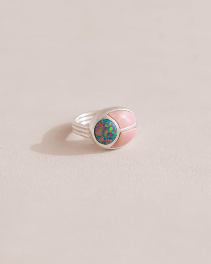 A silver ring featuring a central opal stone flanked by pink opal stones on either side, set against a neutral background.