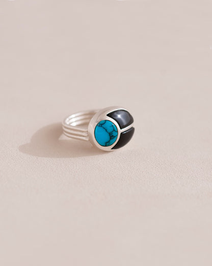 A silver ring featuring a central turquoise stone flanked by onyx stones on either side, set against a neutral background.