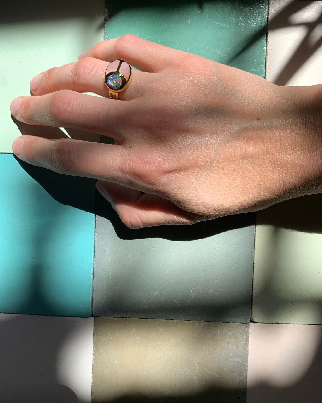 hand wearing a scarab ring in front of green tiles
