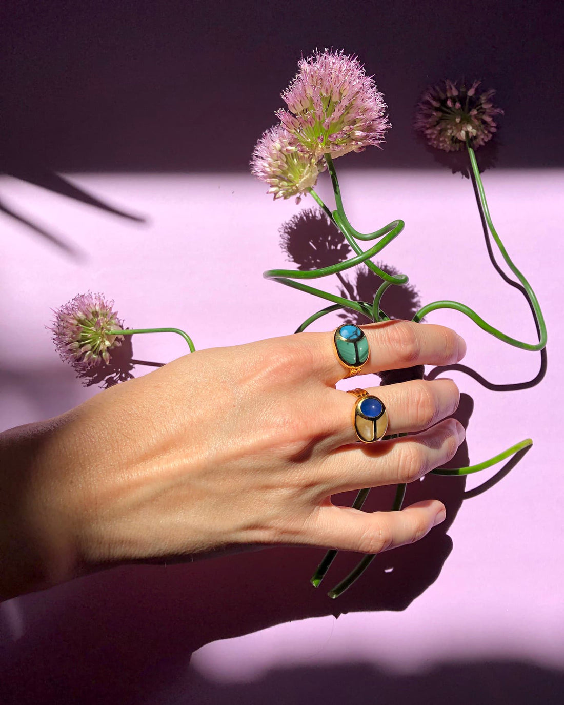hand wearing two scarab rings while holding flowers
