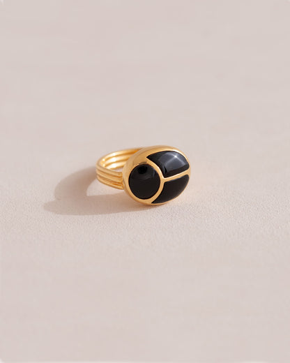 A gold ring featuring a central onyx stone flanked by onyx stones on either side, set against a neutral background.